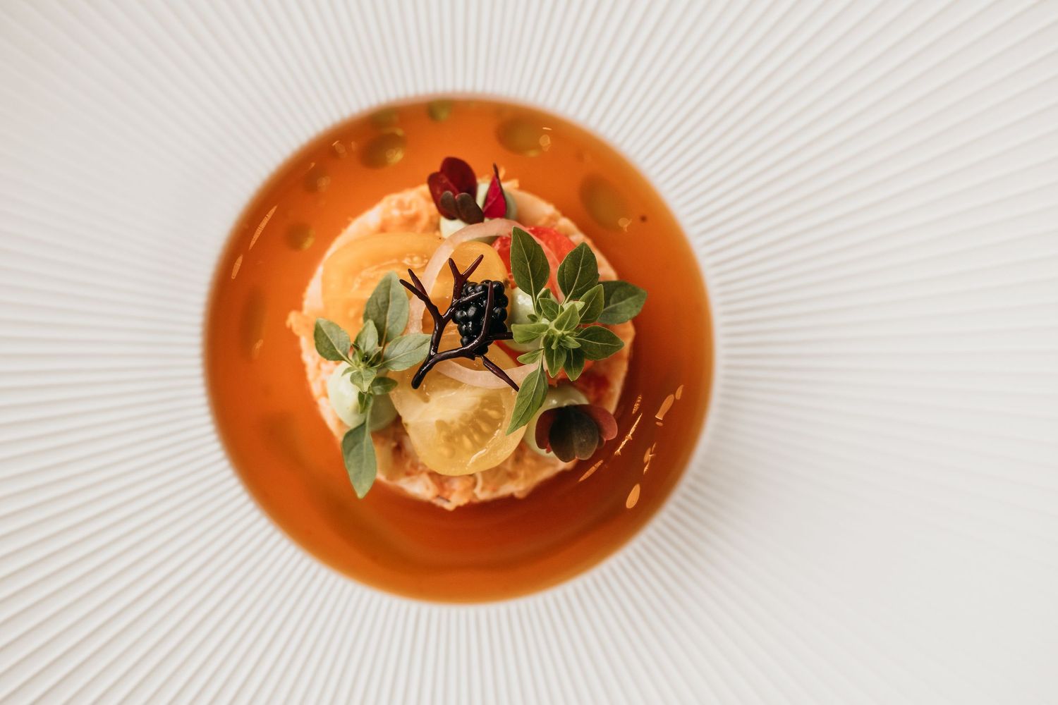 Gourmet dish served on orange plate with fresh herbs, vegetables and decorative garnish in fine dining setting.