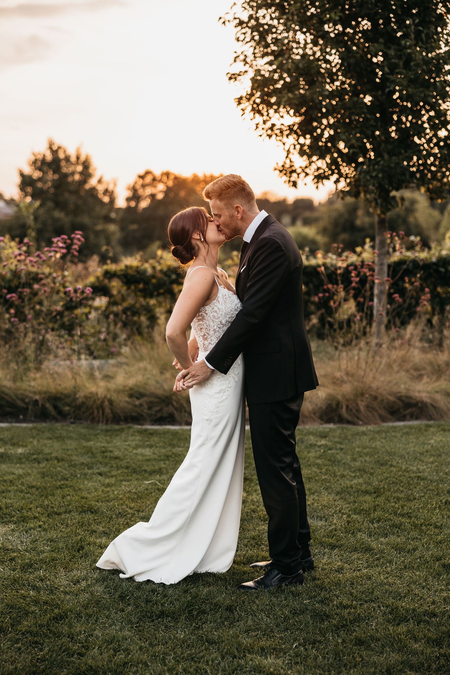 Bride and groom share a passionate kiss at golden hour in a lush garden setting.