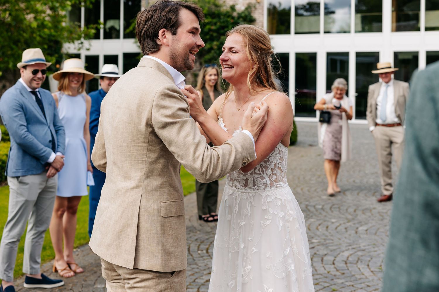 Joyful bride and groom sharing a happy moment outdoors surrounded by wedding guests.