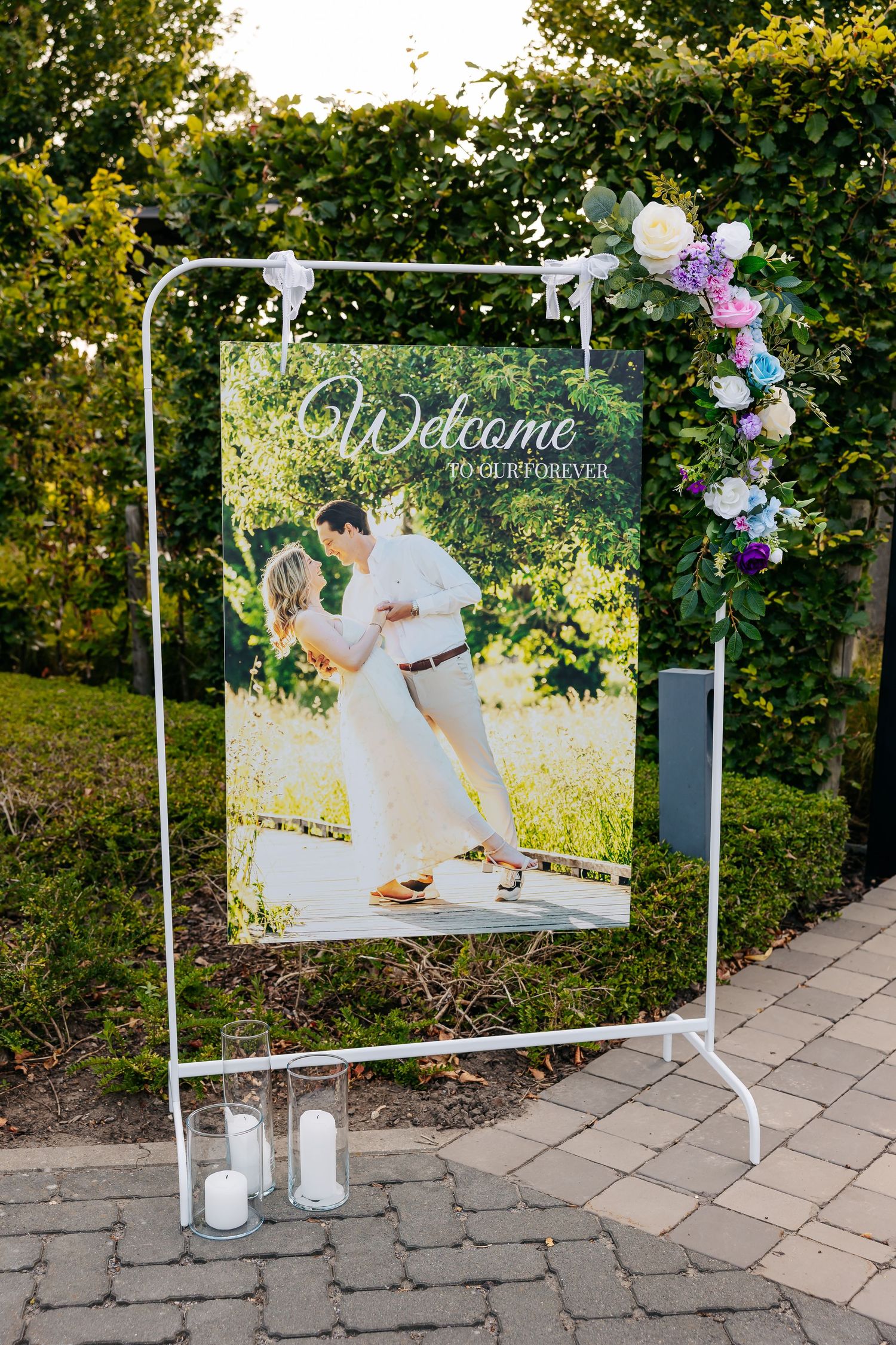 Outdoor wedding welcome sign displaying couple photo surrounded by floral arch.