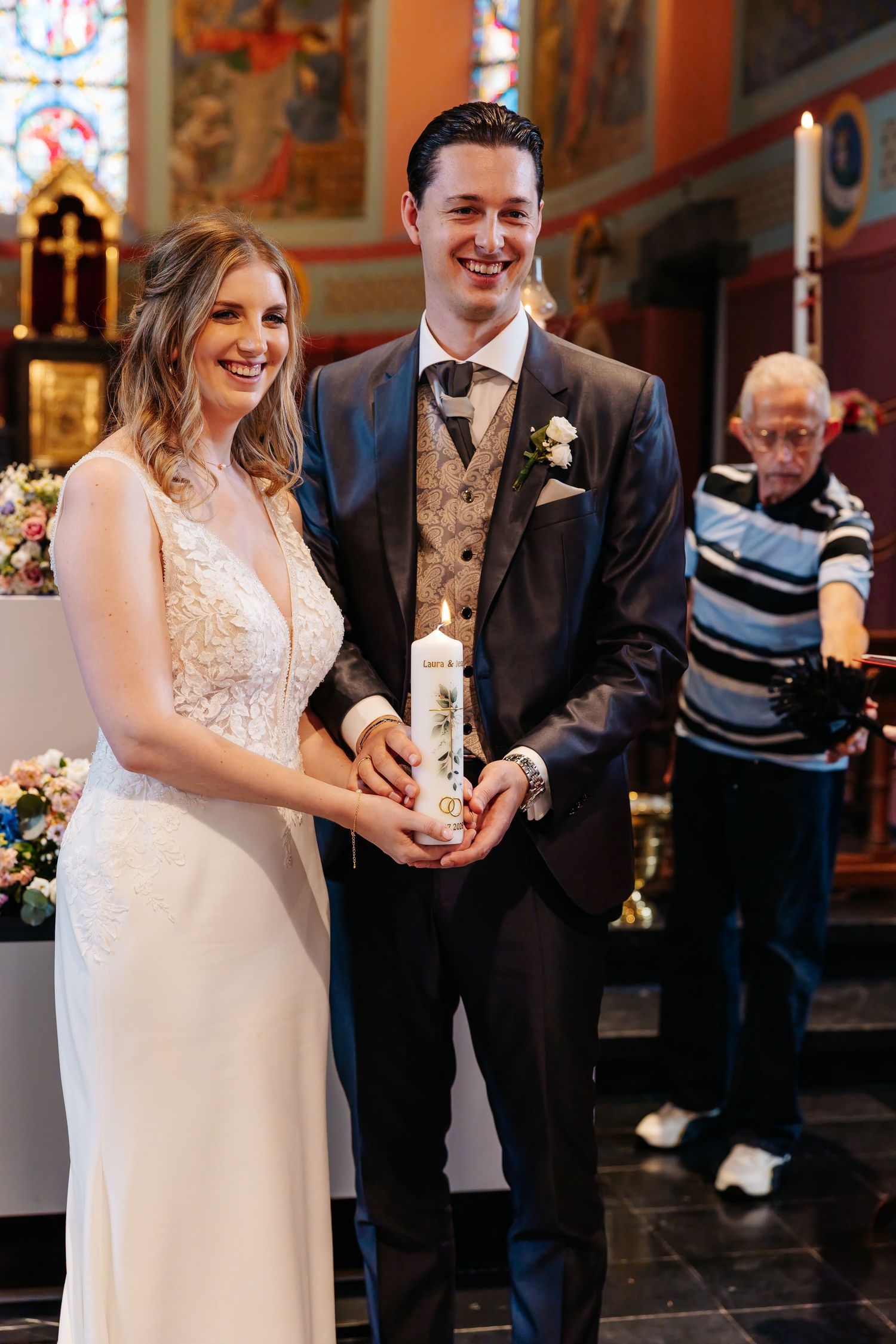 Smiling bride and groom holding a lit unity candle during their church wedding ceremony.