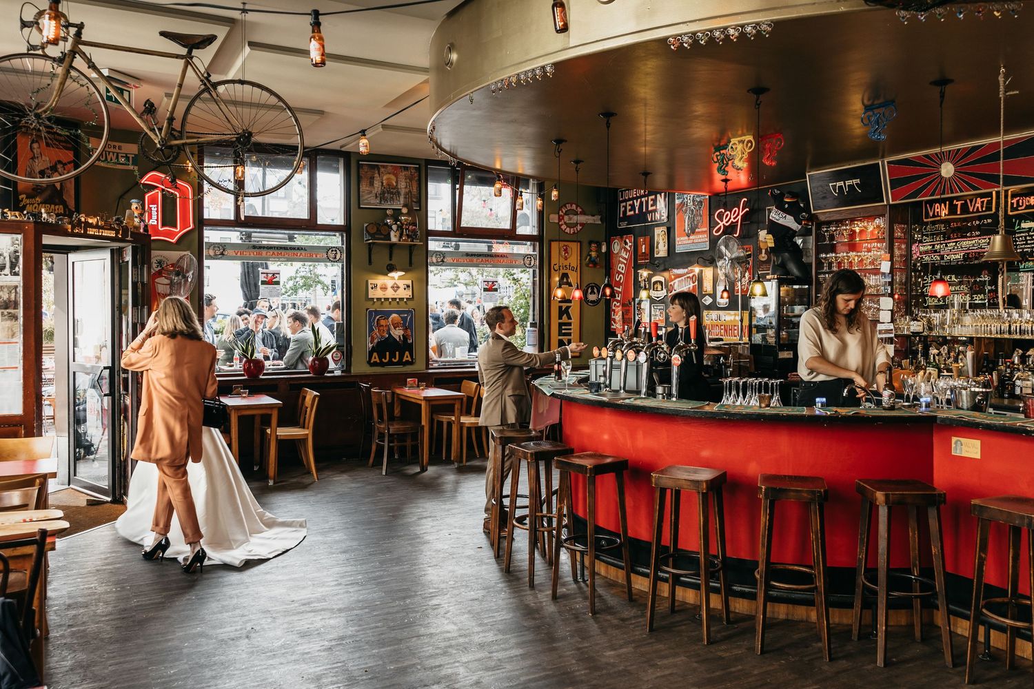 Interior of a stylish bar with red counter, bar stools, hanging bicycle, and neon signs.