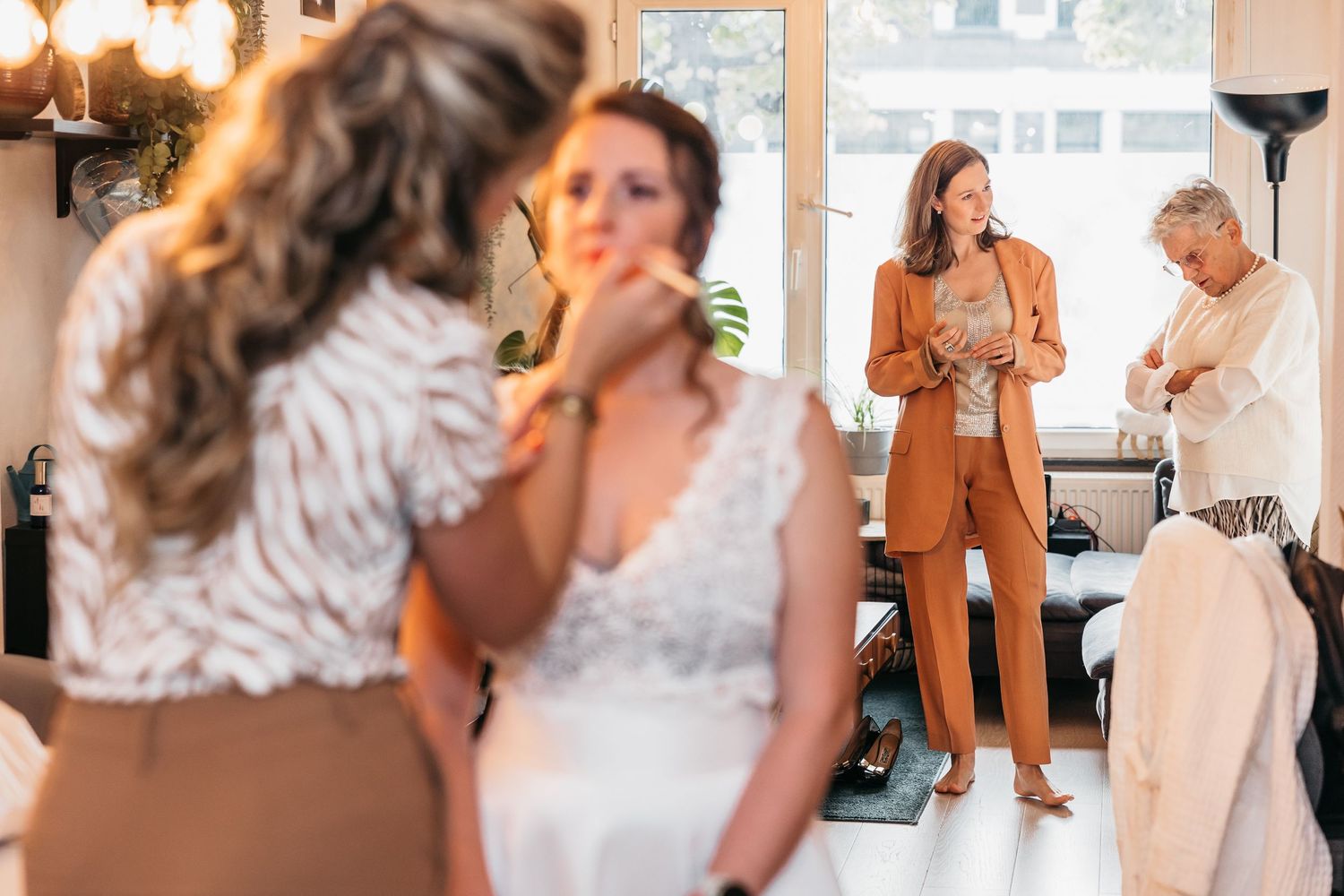 Bride getting makeup done while wedding guests in elegant outfits watch in a bright modern salon.