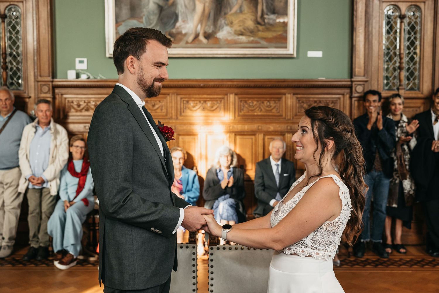 Bride and groom exchange rings and smile at each other during wedding ceremony in elegant historic venue.