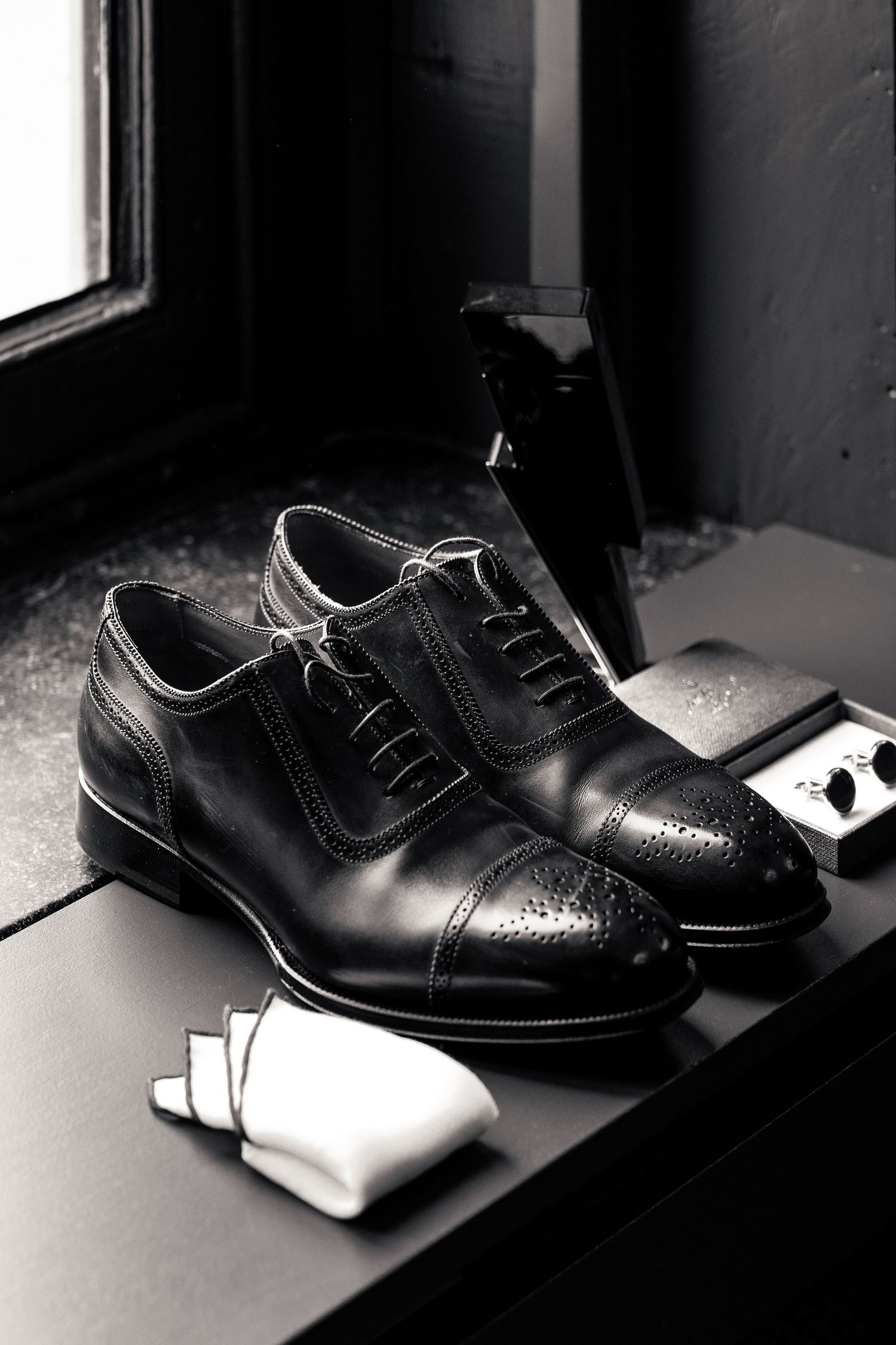 Black and white photo of groom's Oxford brogue shoes with socks and cufflinks.