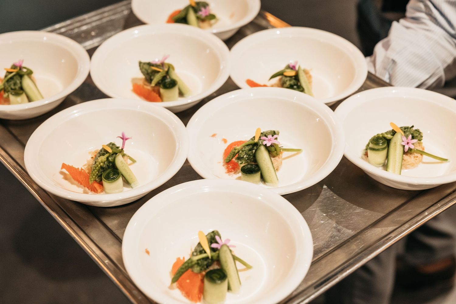 Nine elegantly plated gourmet appetizers with vegetables and garnishes arranged on a silver serving tray.