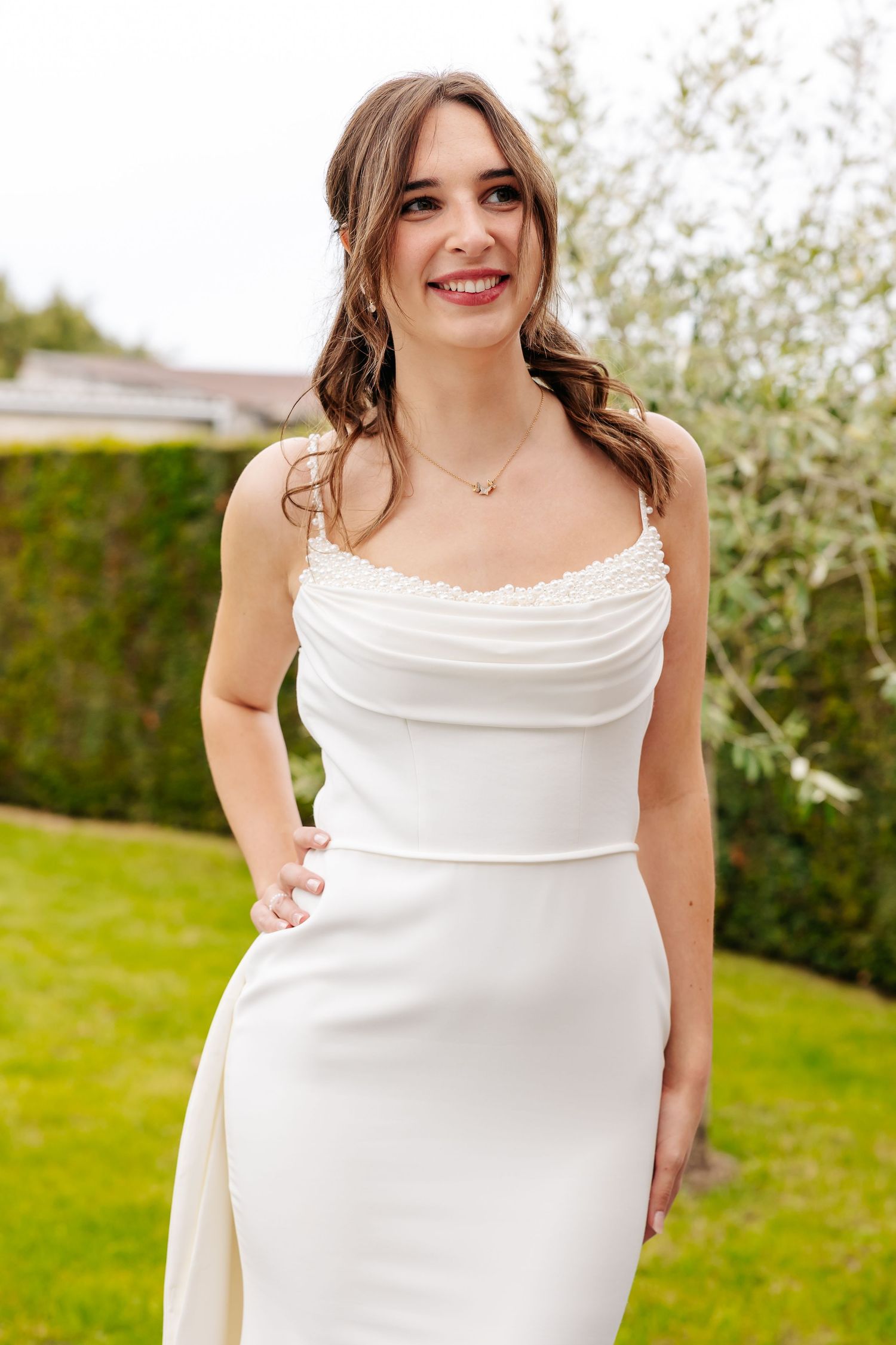 Radiant bride in a cowl-neck white wedding dress smiles joyfully in a garden setting.