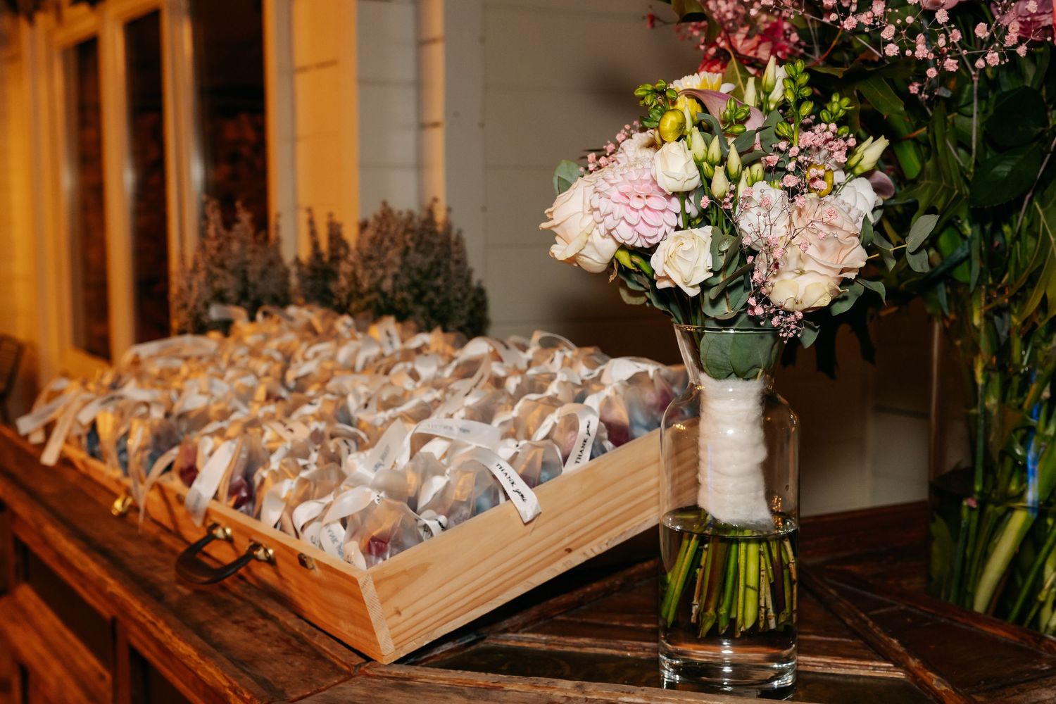 Wedding favor cookies in wooden tray displayed beside a beautiful pink and white bridal bouquet.