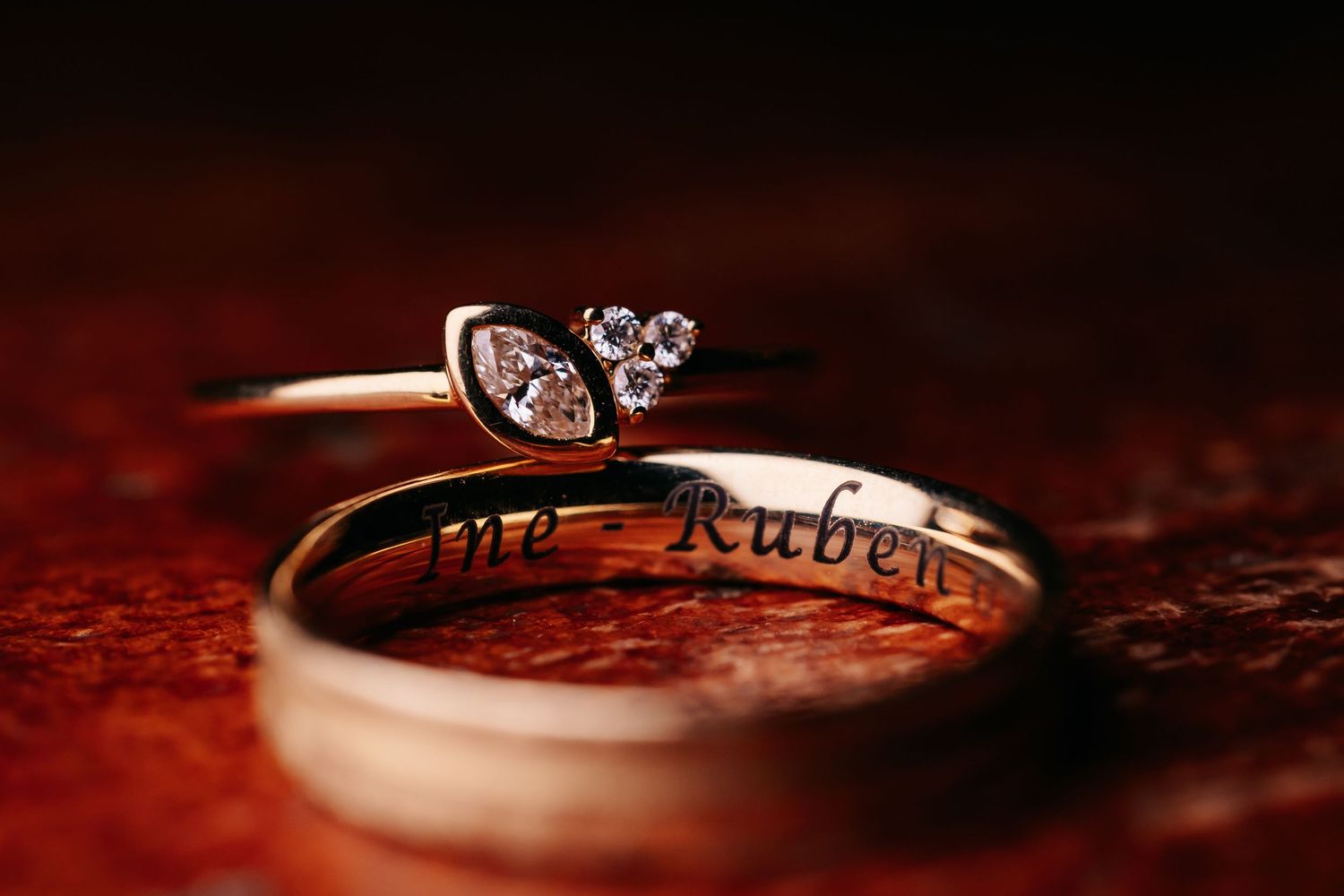 Close-up of engraved wedding bands with diamond engagement ring stacked together on rustic surface.