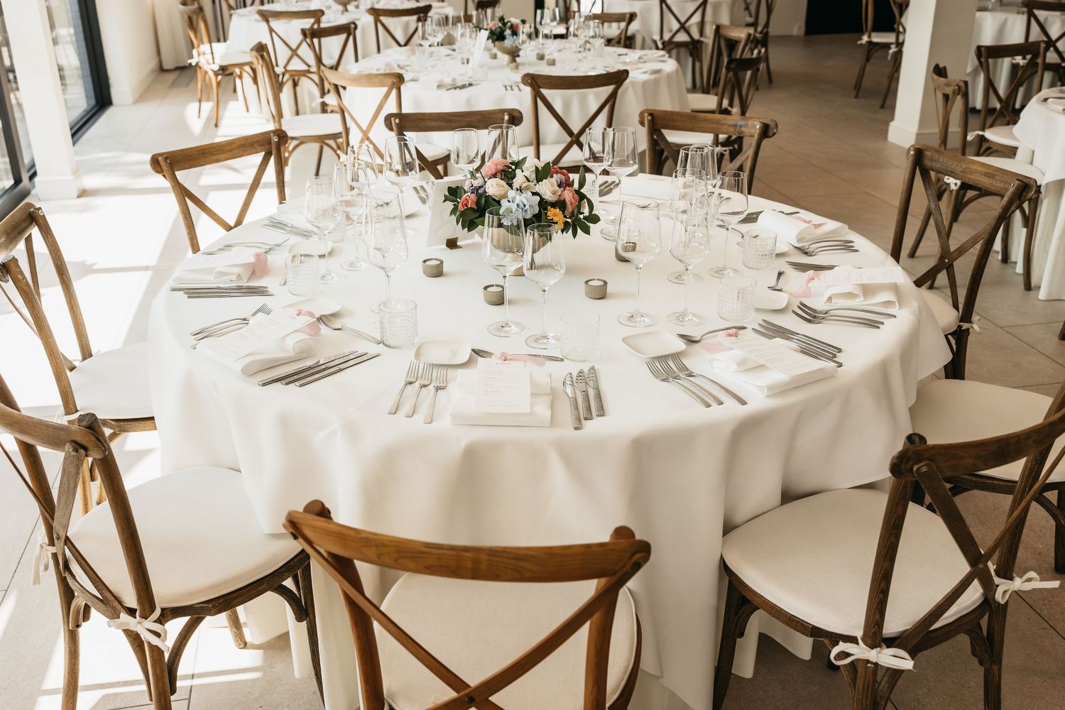 Round wedding reception table set with white linens, crystal glassware, and floral centerpiece.