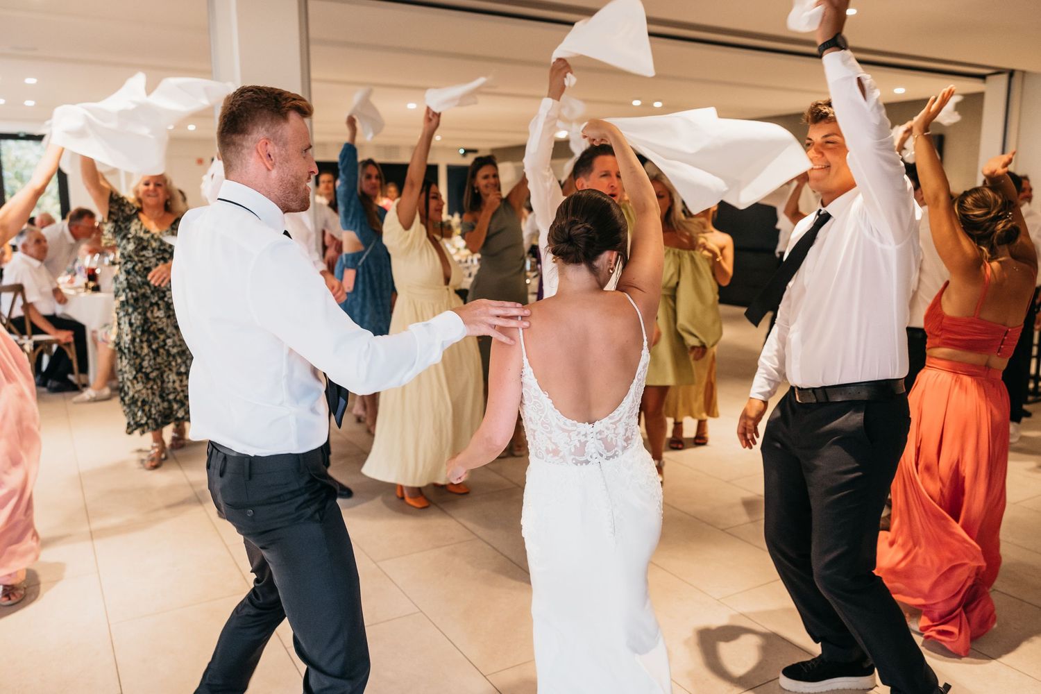 Bride and groom dancing with guests waving white napkins at reception.