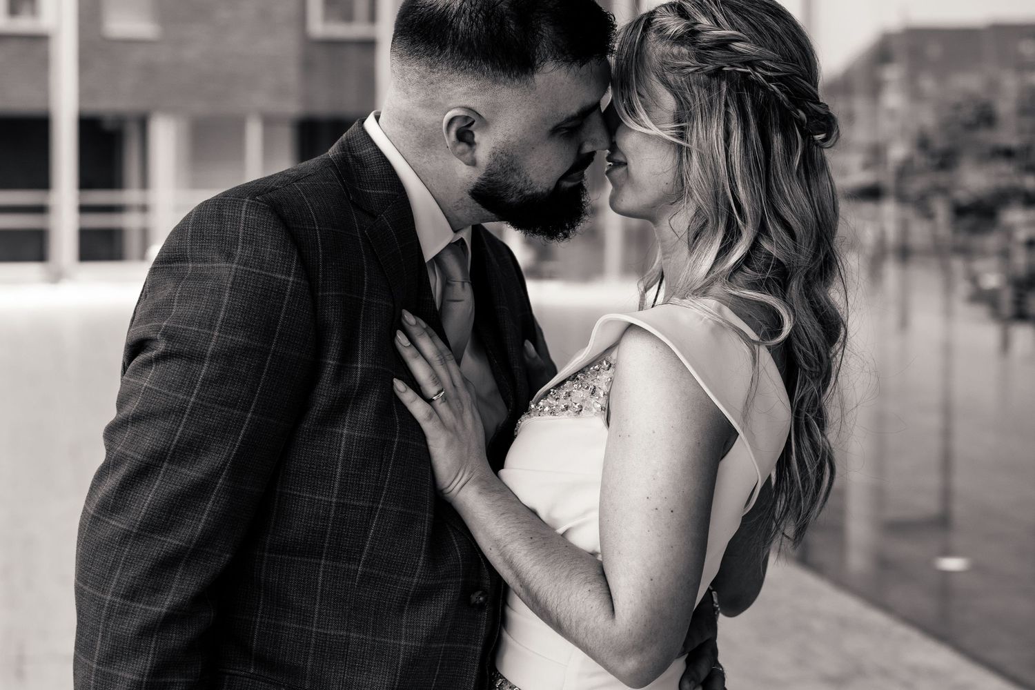 Black and white romantic photo of bride and groom leaning foreheads together in an urban setting.