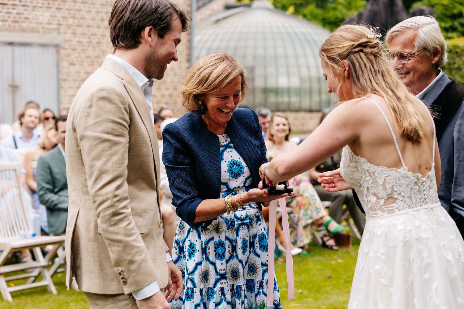 Wedding officiant helping bride and groom exchange rings during outdoor garden wedding ceremony.