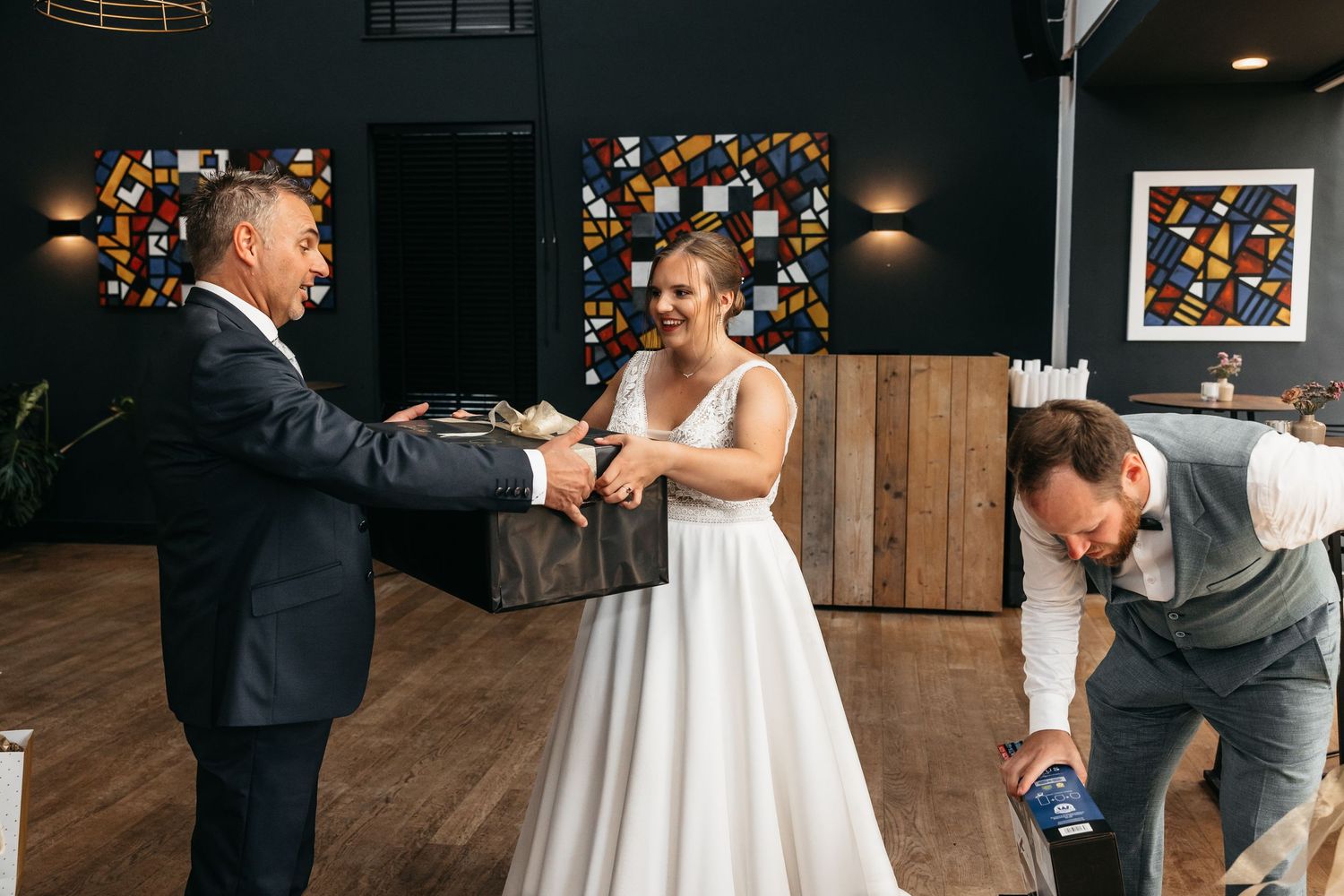 Bride laughing with guests as a surprise wedding gift box is opened in a modern reception hall.