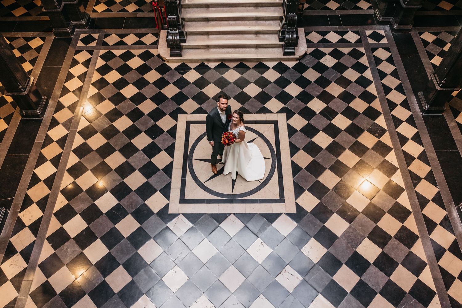 Bird's eye view of wedding couple embracing on classic checkered floor.