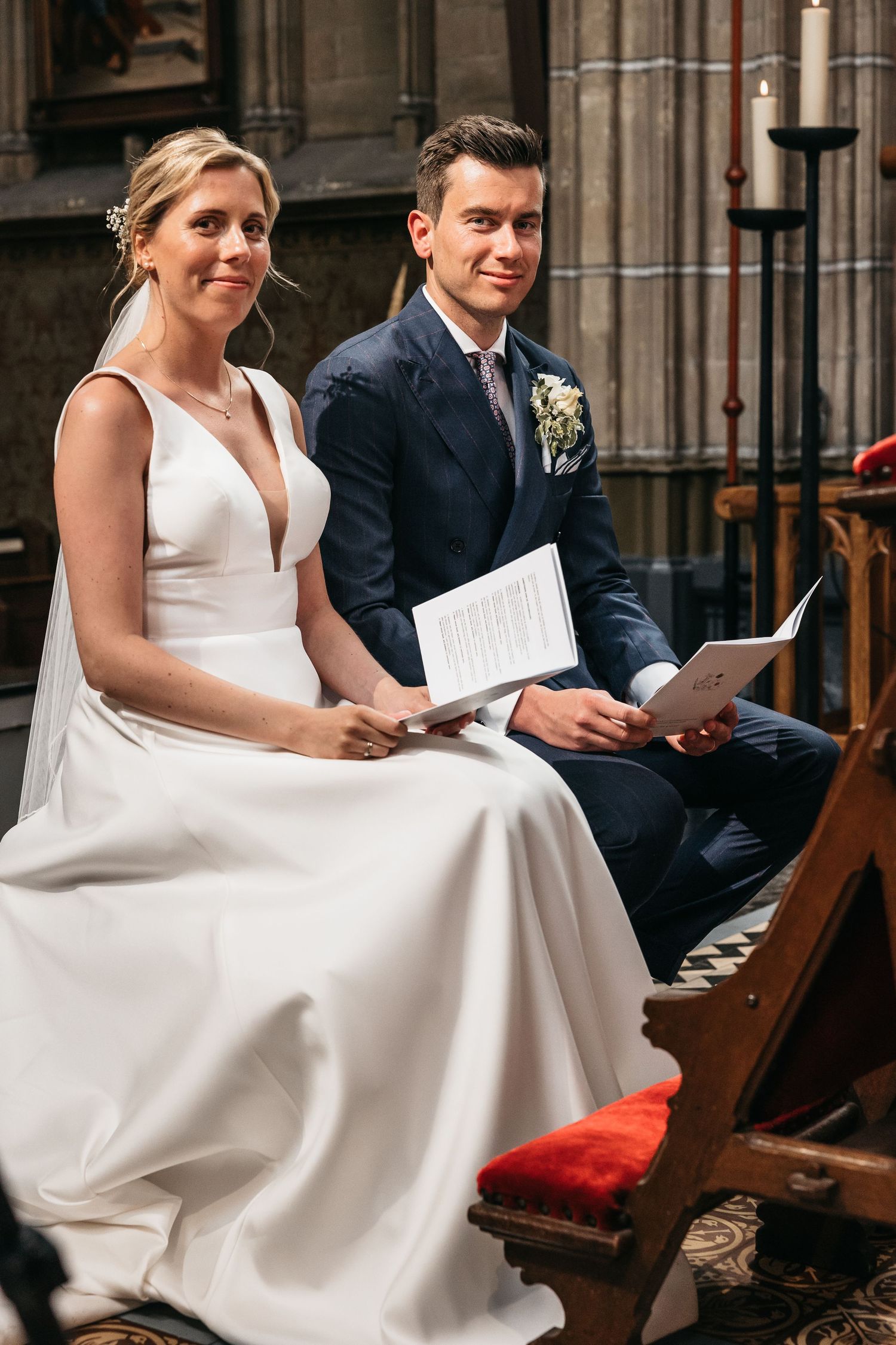 Bride and groom sit together holding ceremony programs during their church wedding service.