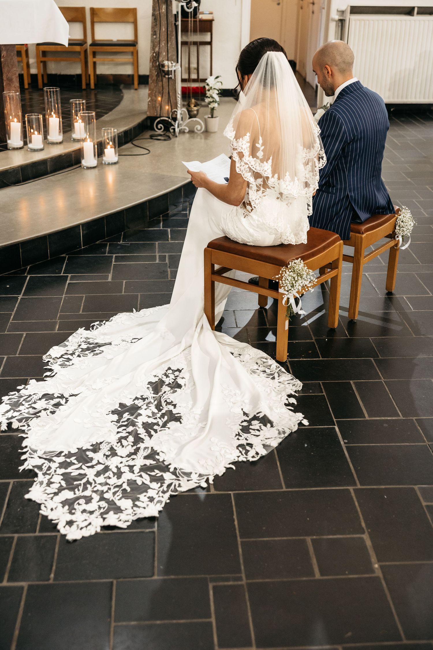 Bride and groom seated at church altar, bride's intricate lace veil and train spread on floor.