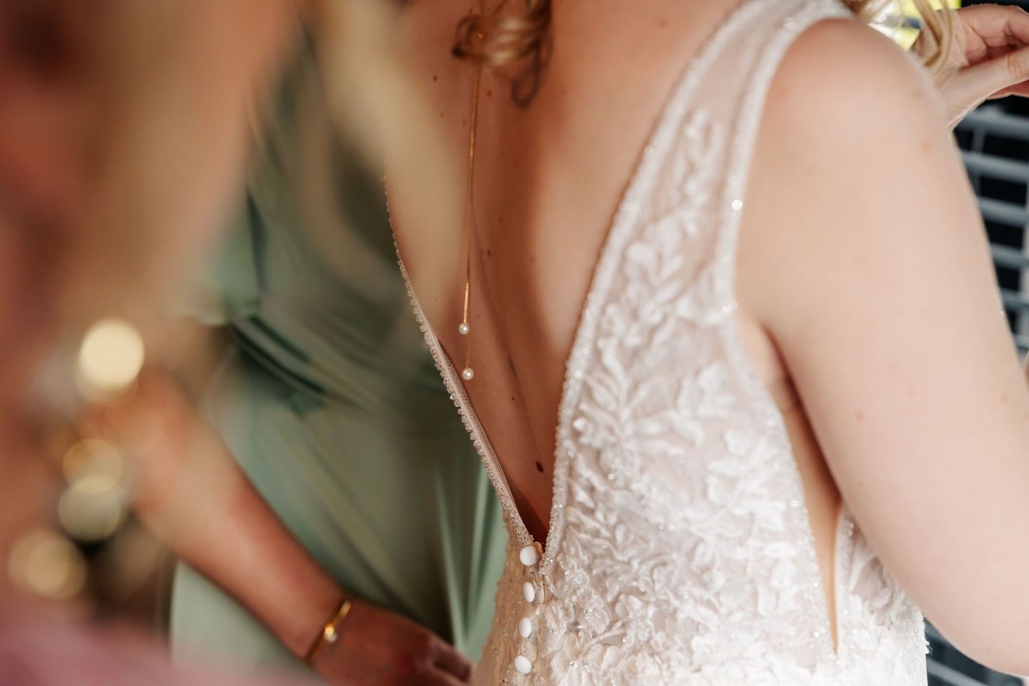 Detail shot of a gold drop pearl back necklace resting against the lace open back of a bridal gown.