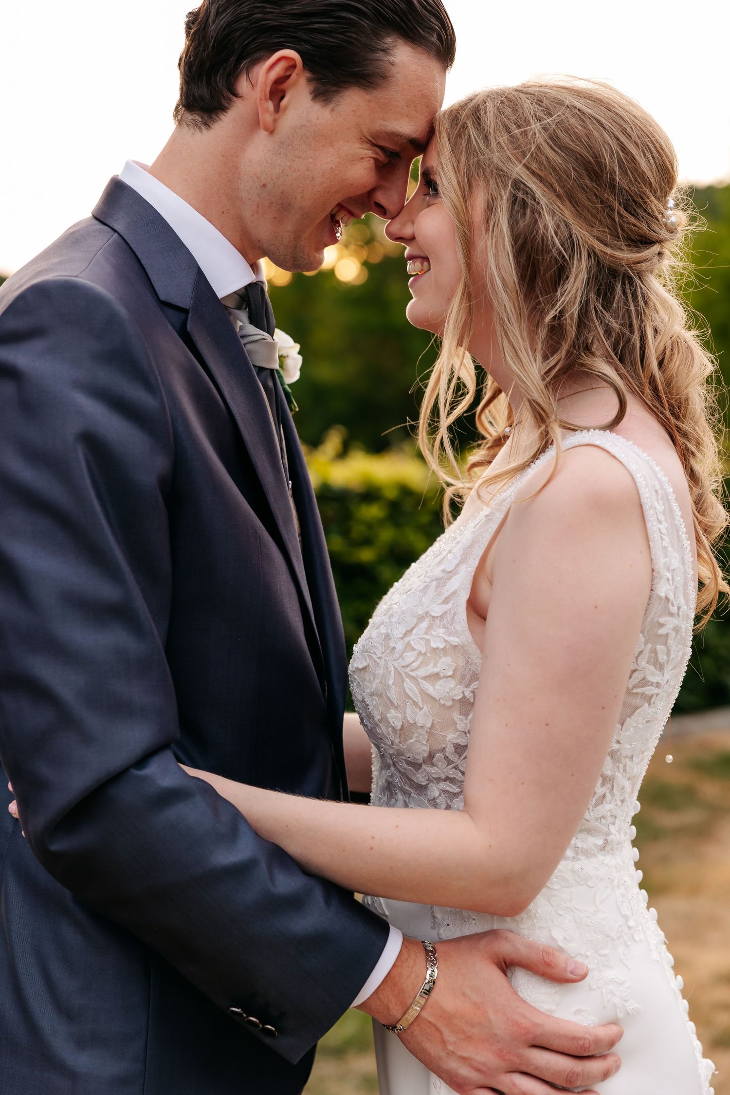 Bride and groom share an intimate moment touching foreheads and smiling in golden hour light.