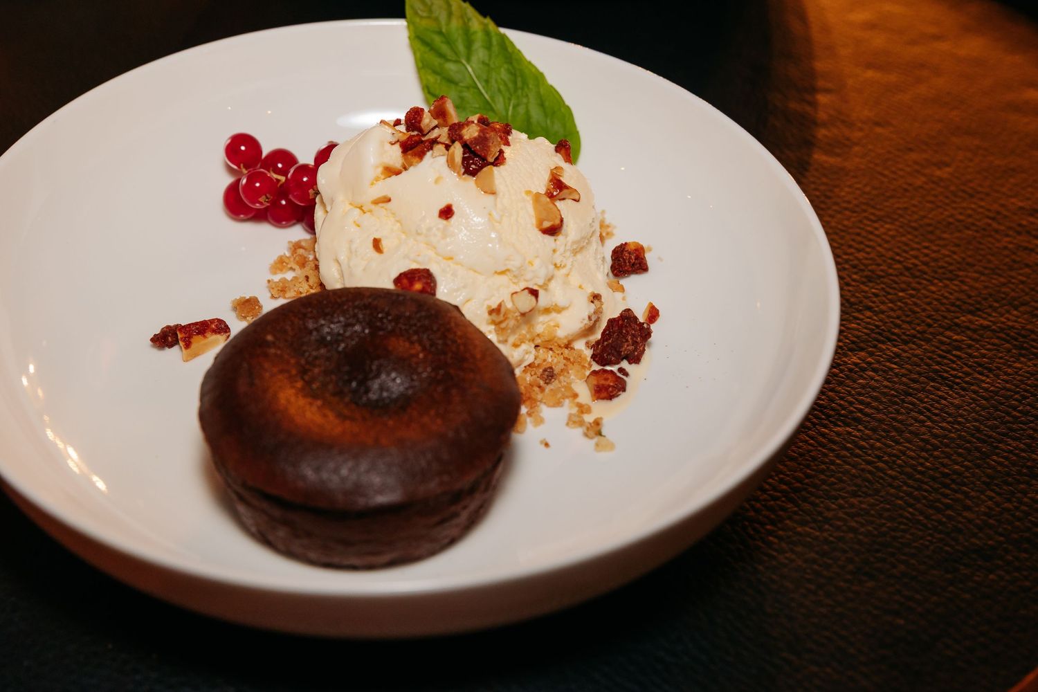 Chocolate lava cake with vanilla ice cream, red currants, and nuts on a white plate.
