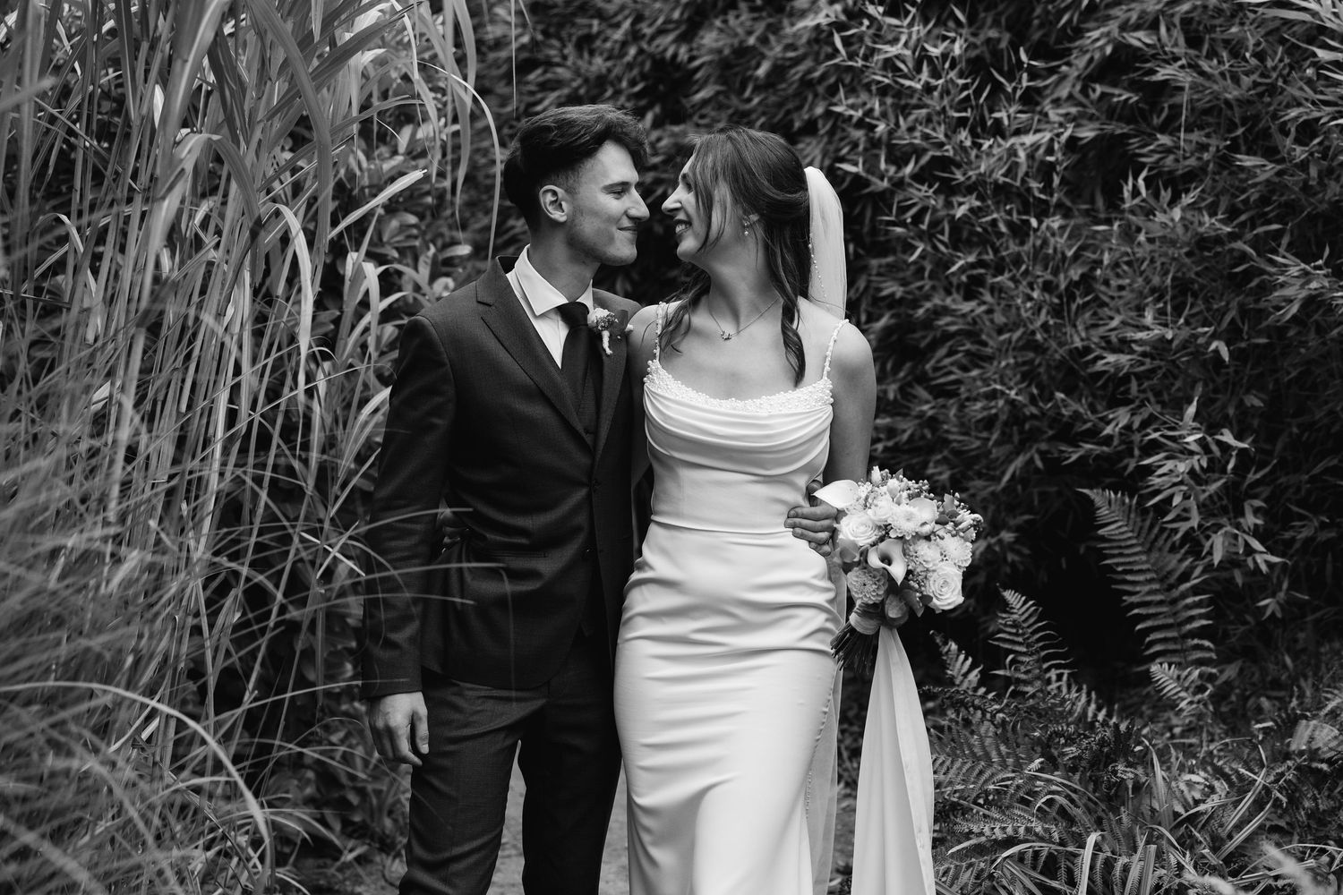 Black and white romantic portrait of bride and groom gazing at each other in a lush garden.