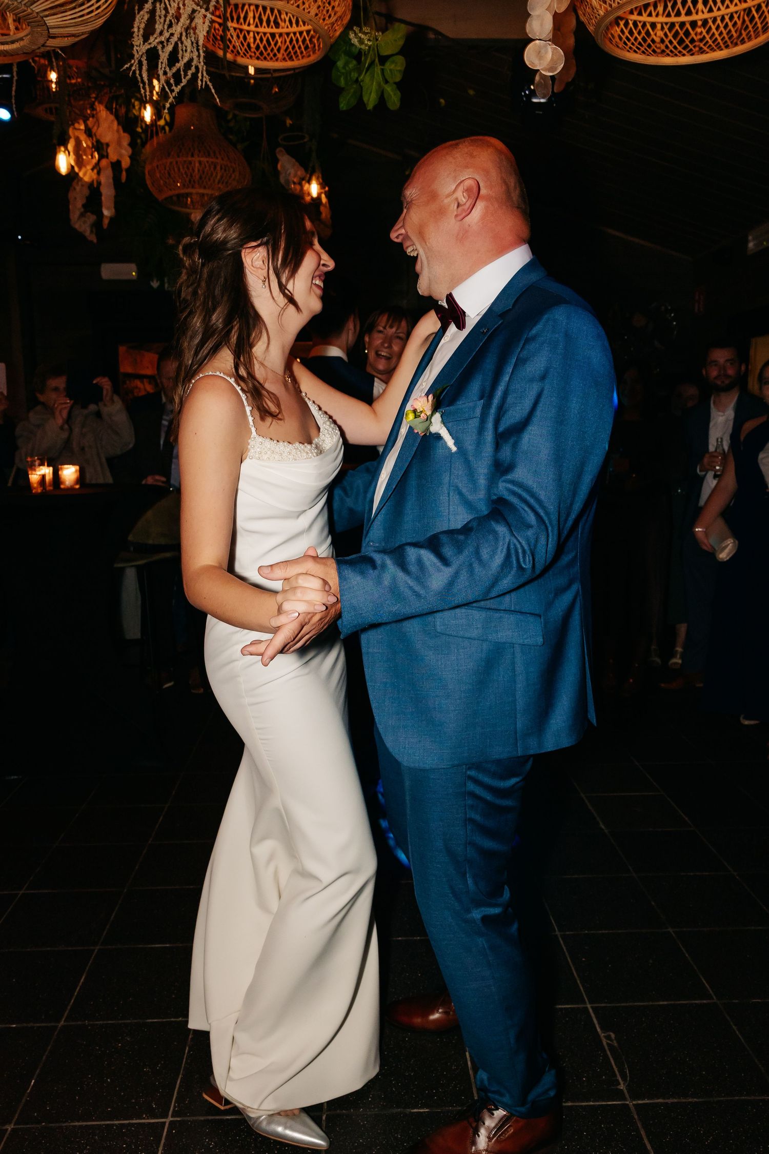 Bride and man in blue suit laughing together during a dance at wedding reception.
