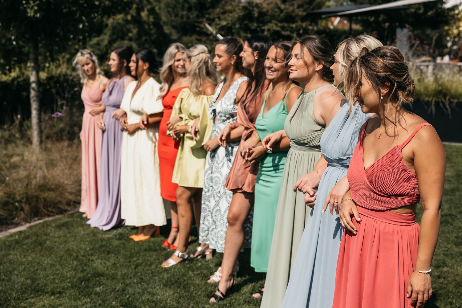 Group of bridesmaids in colorful mismatched dresses standing together outdoors at a wedding.