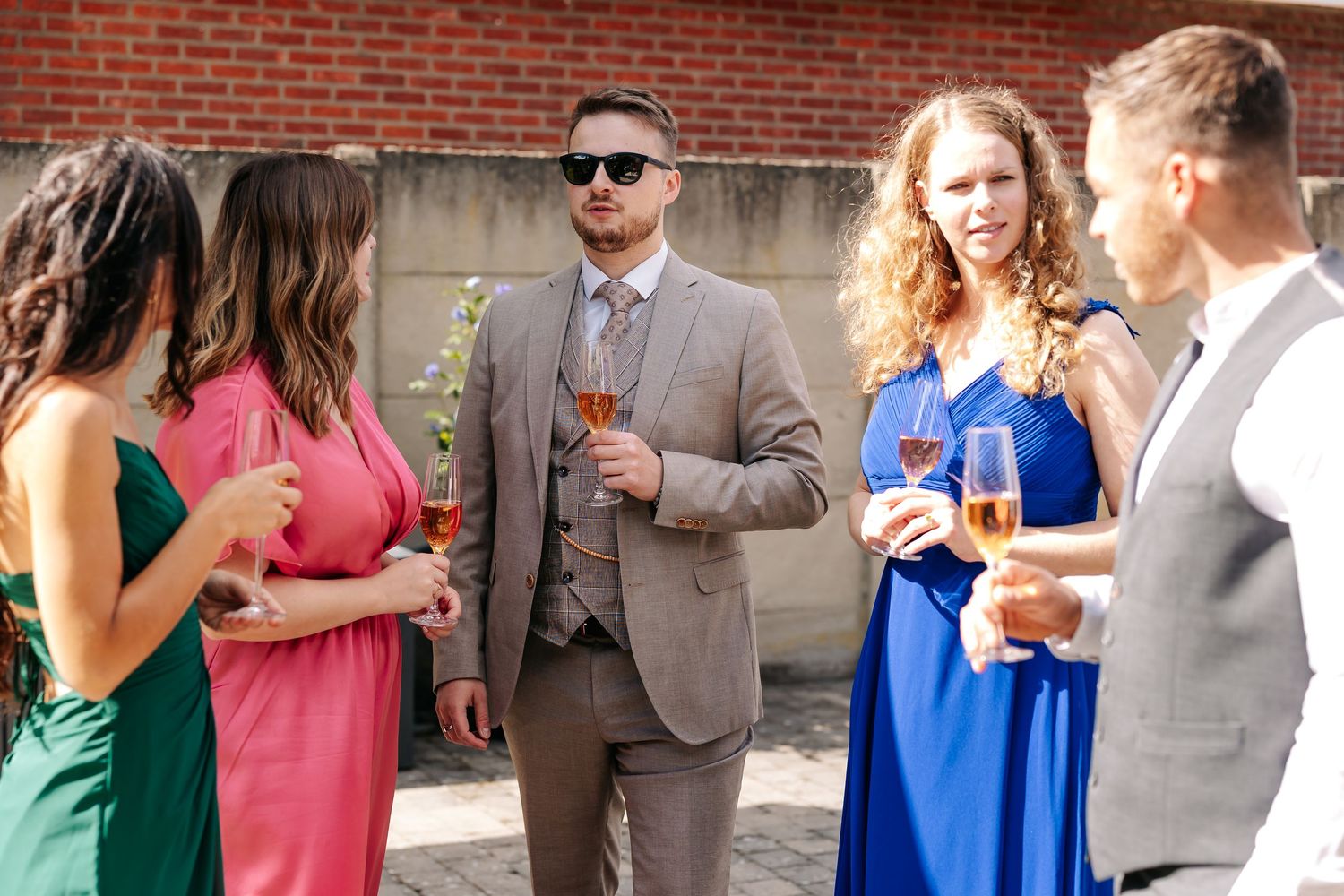 Wedding guests socializing and drinking champagne at outdoor reception.