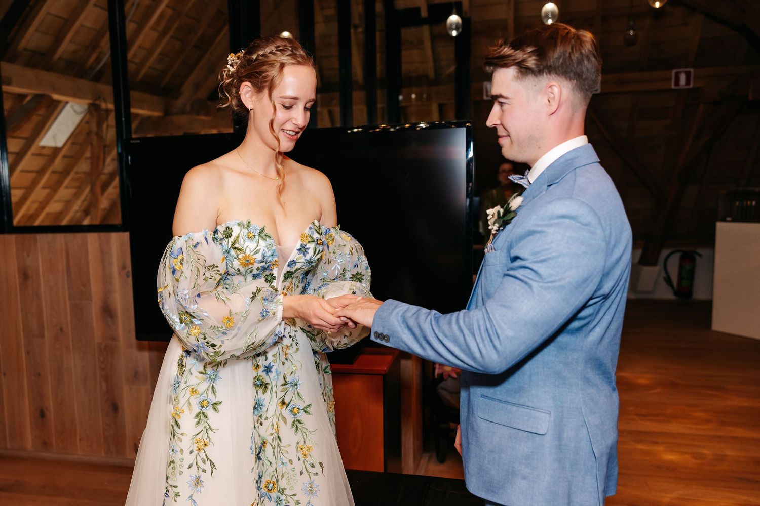 Smiling bride and groom hold hands after exchanging rings during rustic barn wedding ceremony.