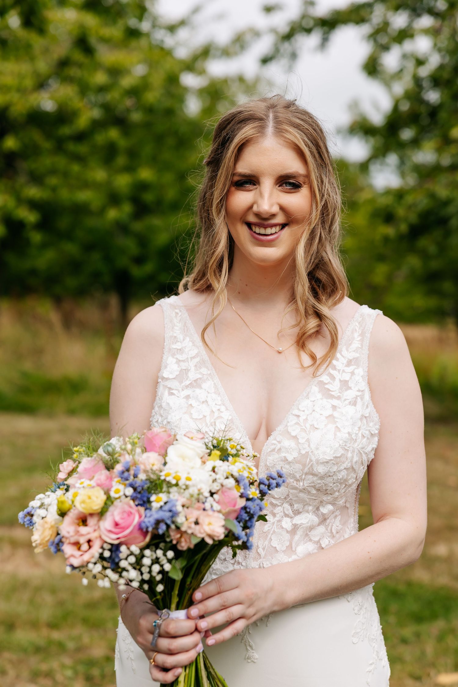 Happy bride in a lace wedding dress smiling while holding a colorful floral bouquet.