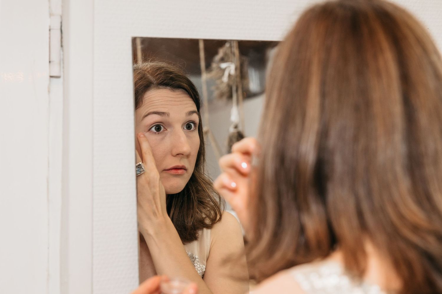 Bride examining her makeup in a mirror during wedding day preparations.