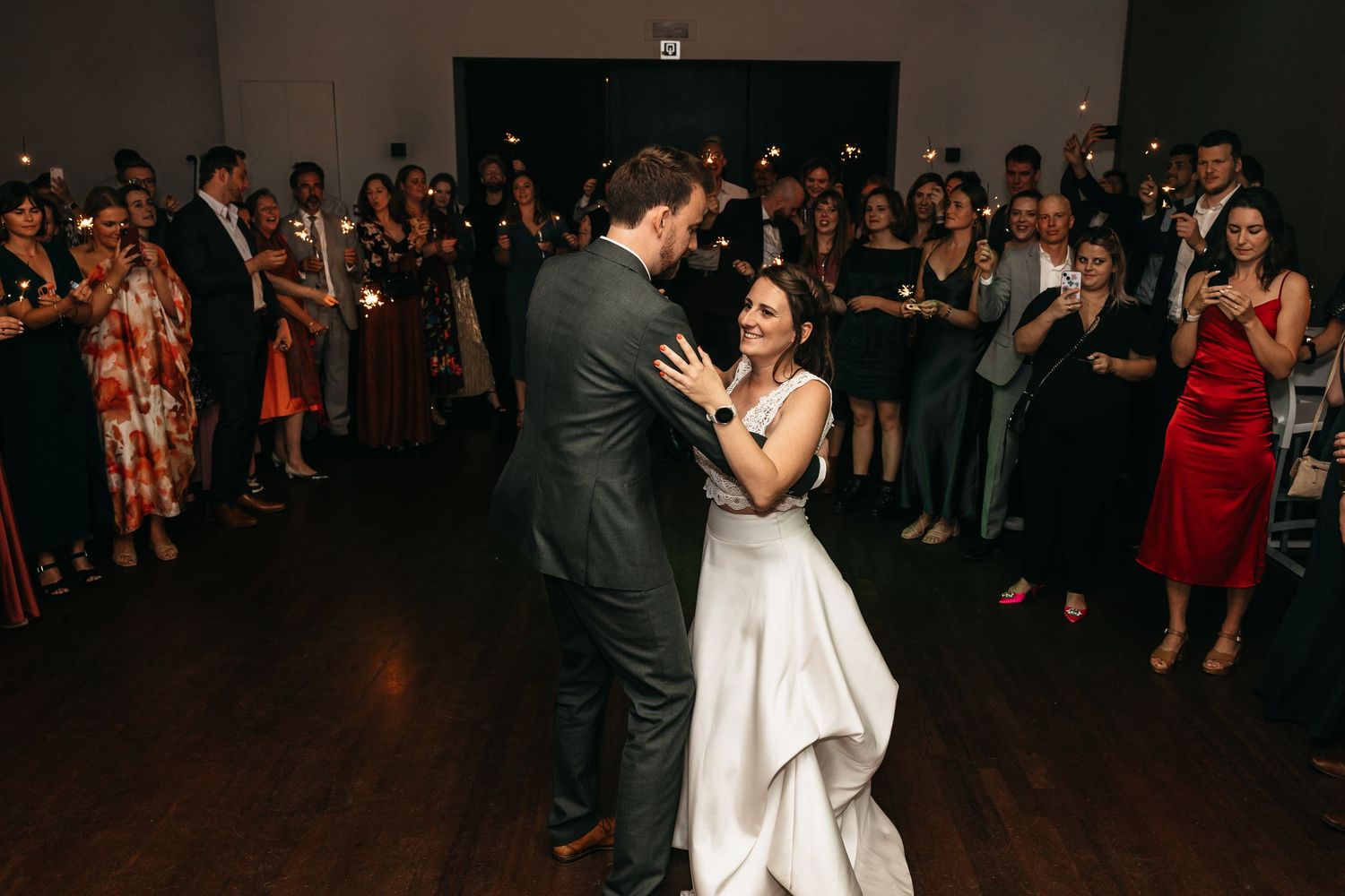 Newlyweds share romantic first dance while wedding guests hold sparklers in background.