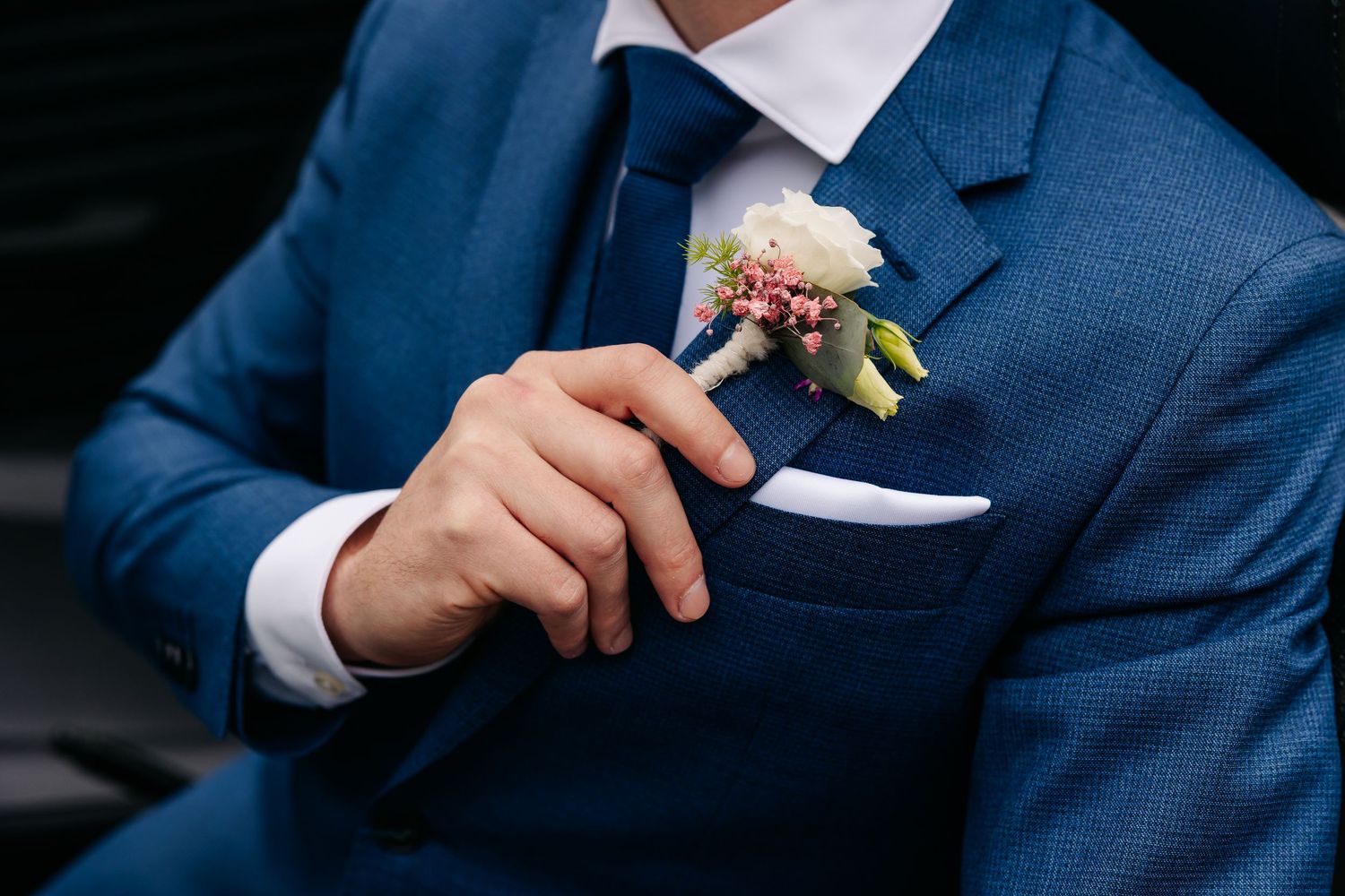 Groom in blue suit with elegant white rose and pink wax flower boutonniere on jacket lapel.