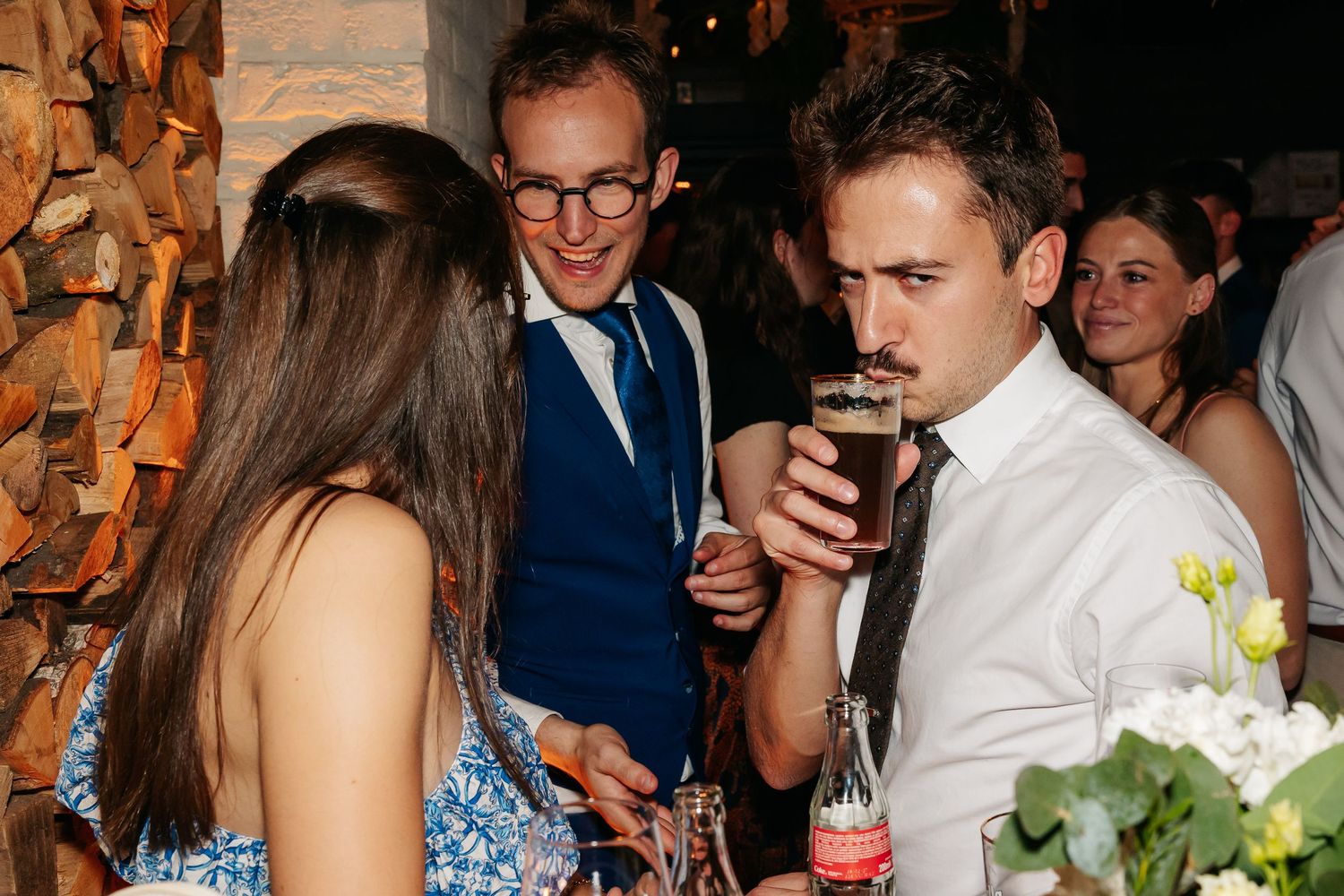 Wedding guests in formal attire socializing and drinking at reception.