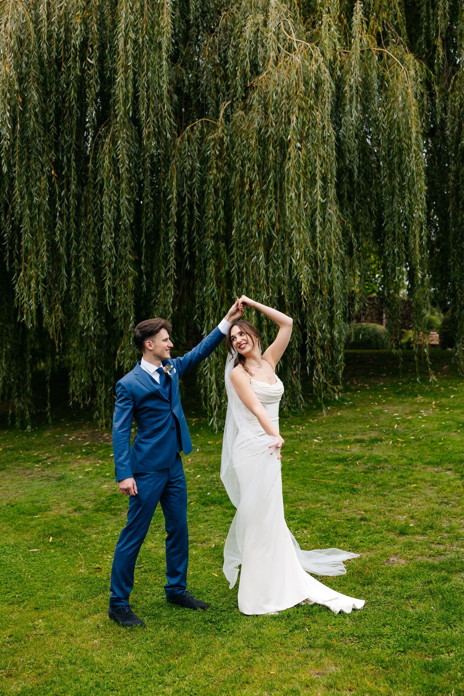 Bride and groom dancing joyfully under a weeping willow tree on their wedding day.