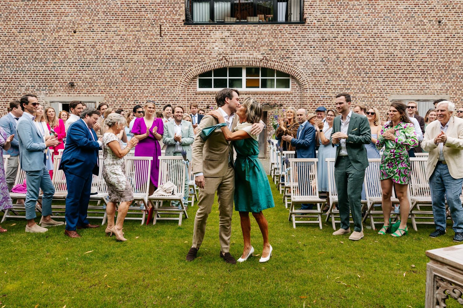 Newlyweds share first dance embrace while wedding guests cheer and applaud outside brick venue.