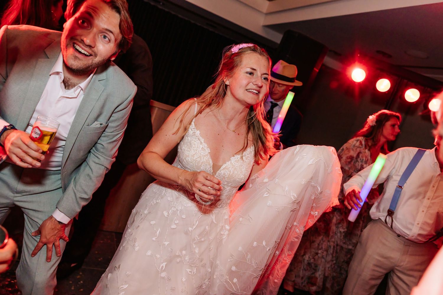 Bride in floral lace wedding gown dances and smiles joyfully at her lively wedding reception party.