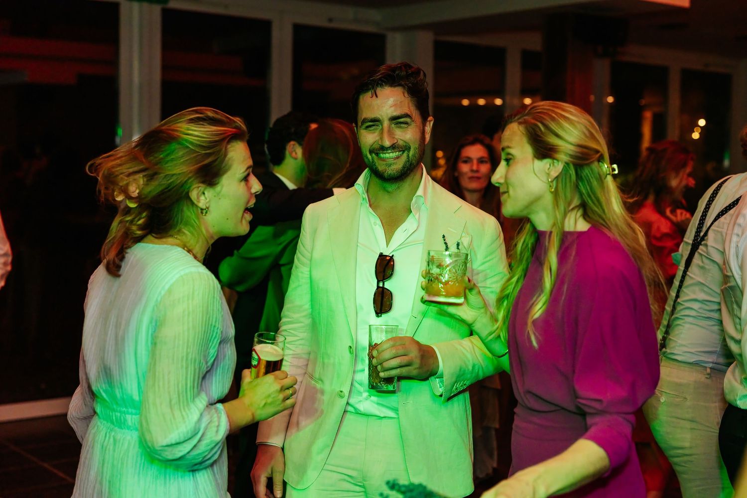 Three elegantly dressed guests socializing under green ambient lighting at a wedding reception party.
