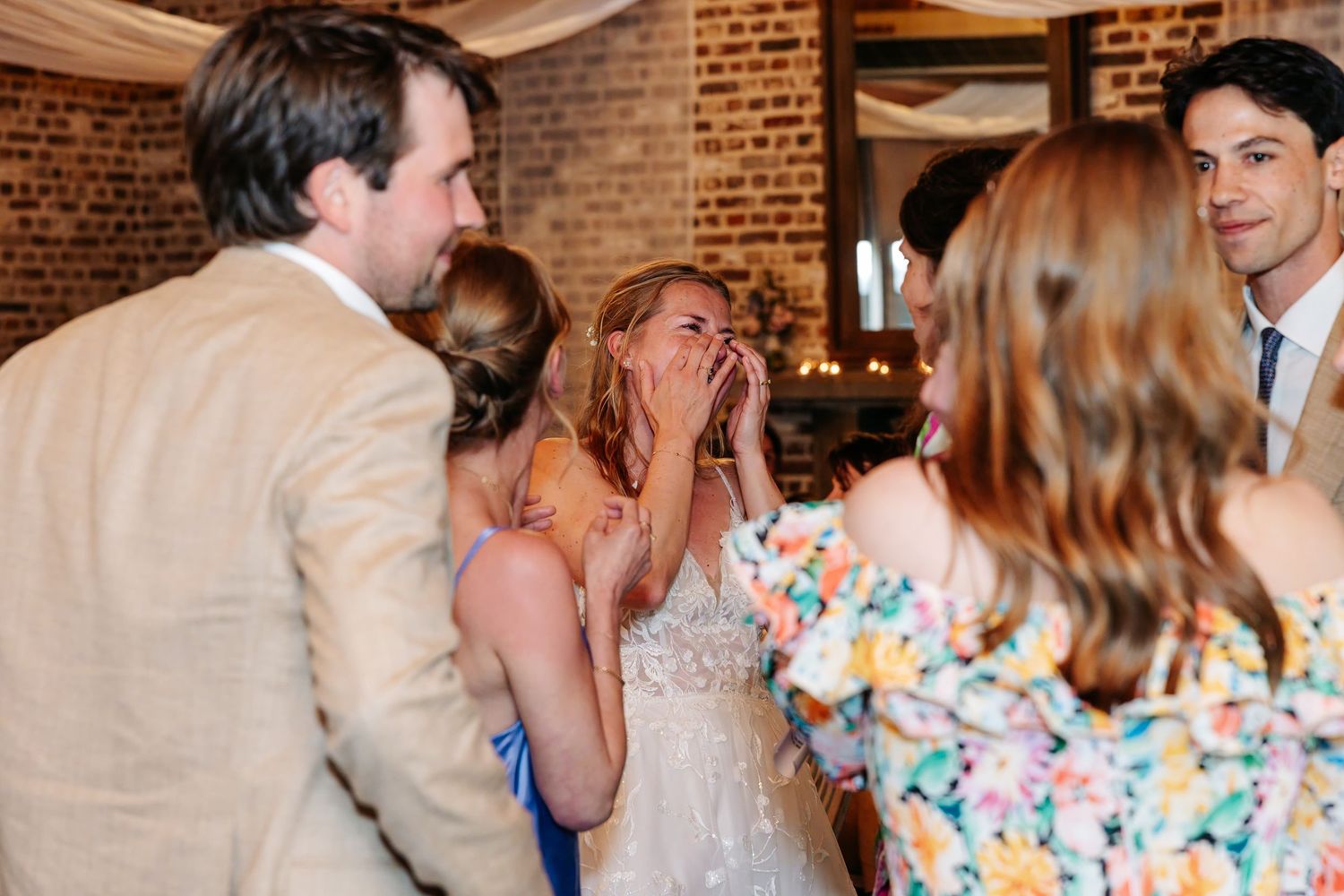 Bride covers her mouth in surprise while chatting with guests at wedding reception.