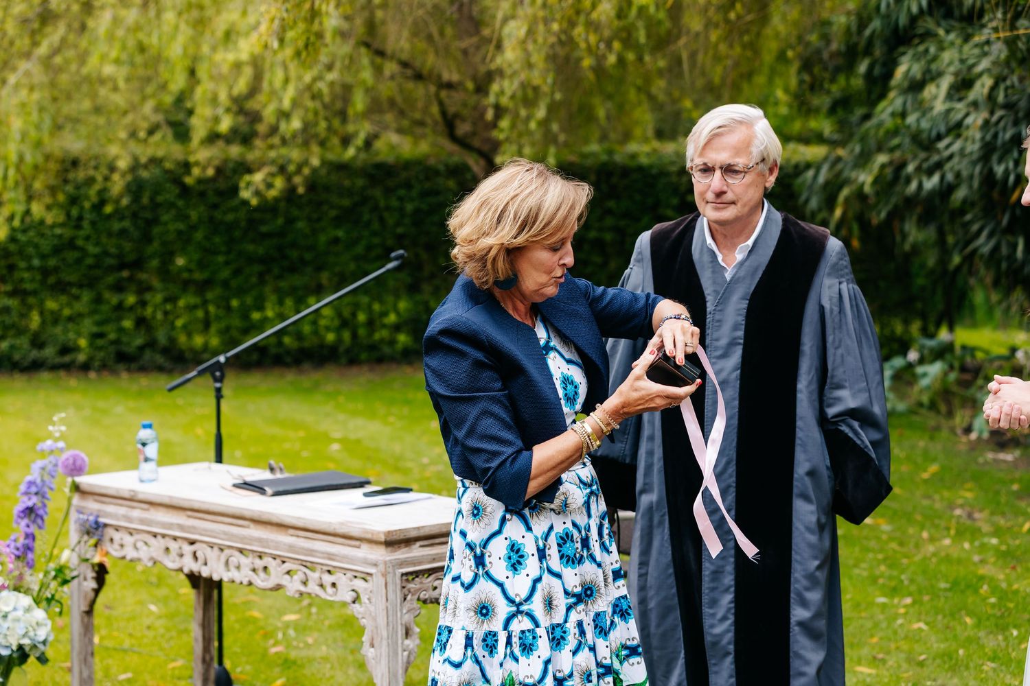 Wedding officiant assists a woman with a ribbon ritual at an elegant outdoor garden ceremony.