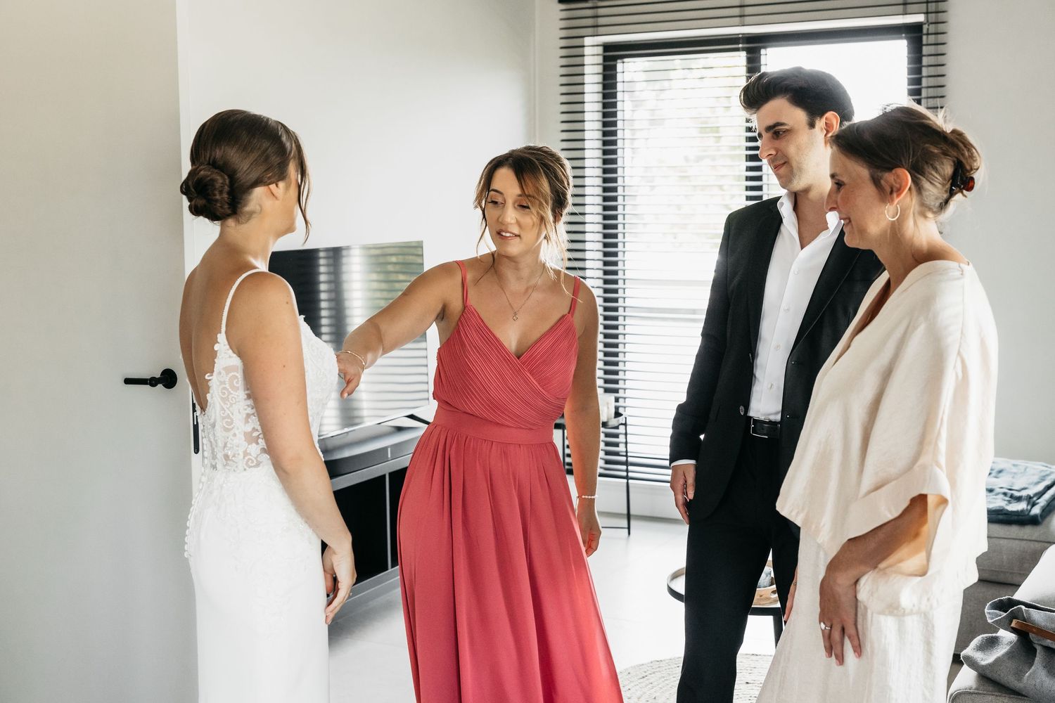 Bride in wedding gown receiving admiring reactions from bridesmaids and family during bridal preparations.