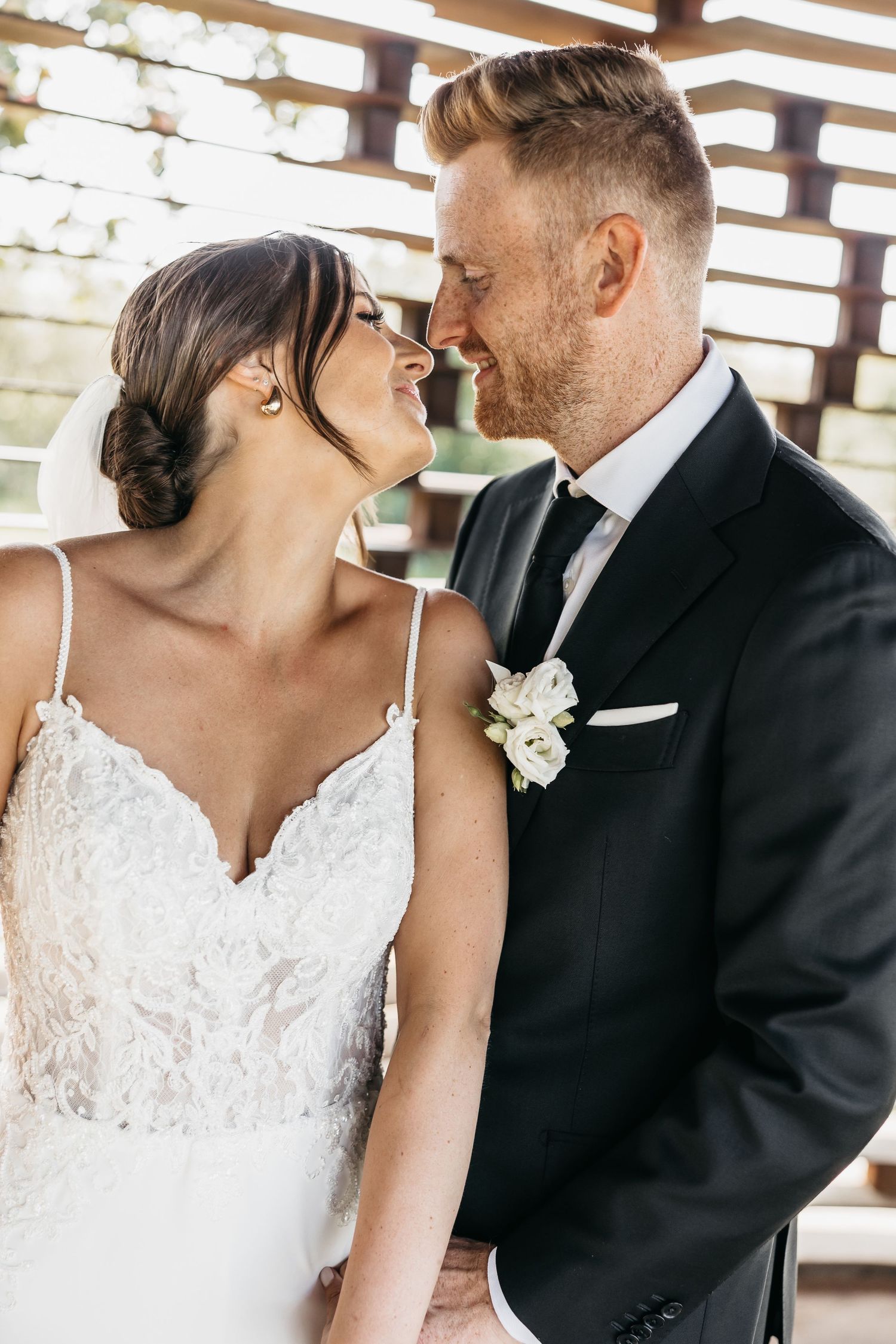 Bride and groom gazing at each other lovingly, groom wearing a black suit with white boutonniere.