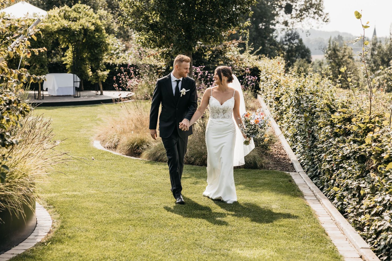 Bride and groom walk hand in hand across a manicured lawn at a beautiful garden wedding.