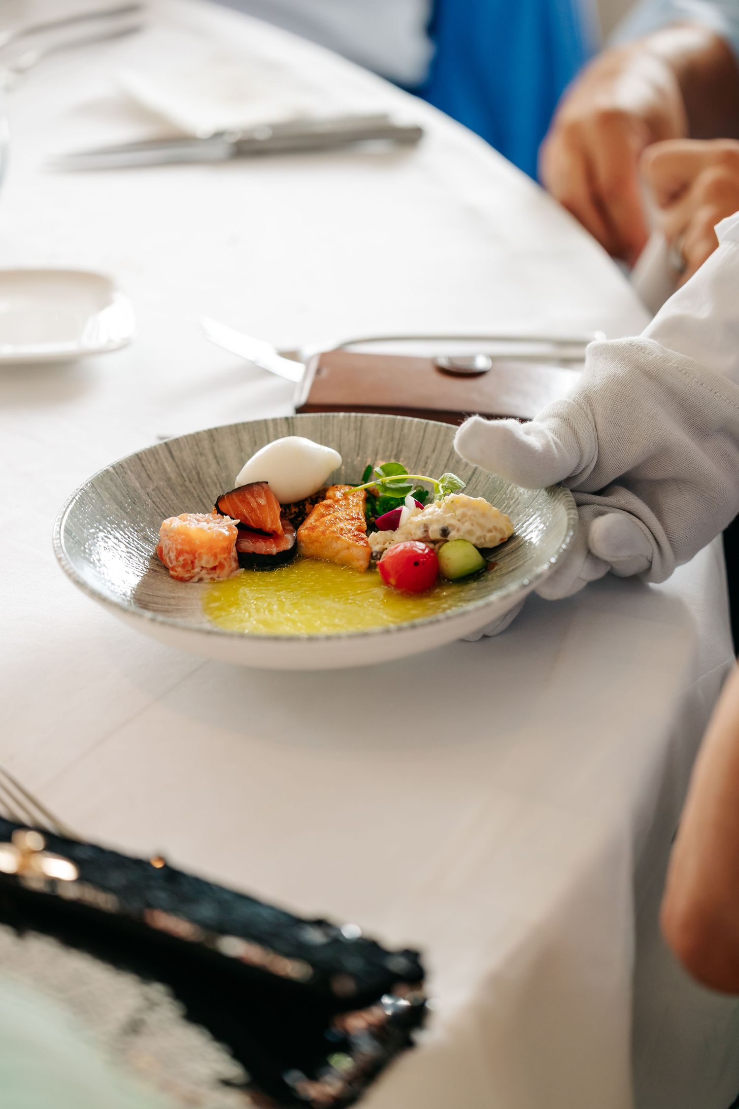 White-gloved server presents elegantly plated gourmet dish with colorful ingredients at wedding reception.