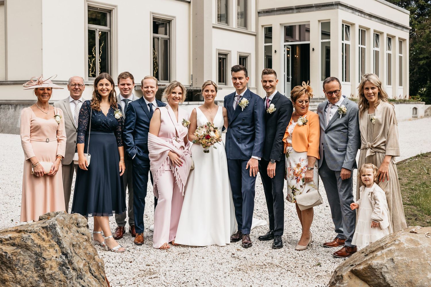 Large wedding family group portrait taken outside an elegant white manor house on a sunny day.