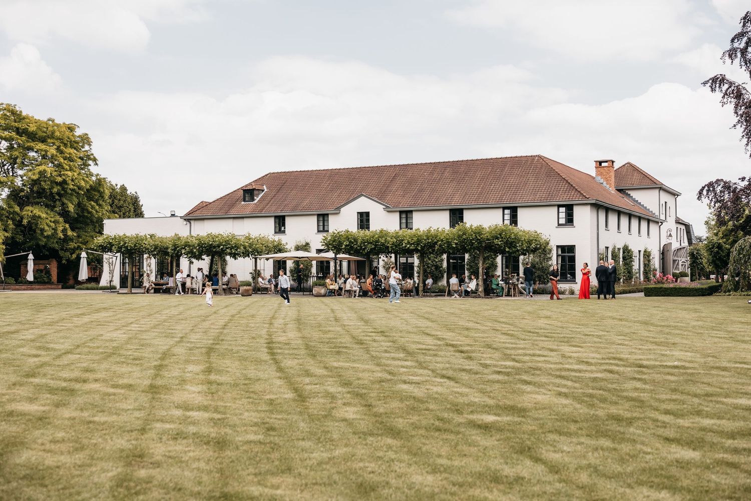 Elegant white country house wedding venue with a vast green lawn and guests mingling outside.