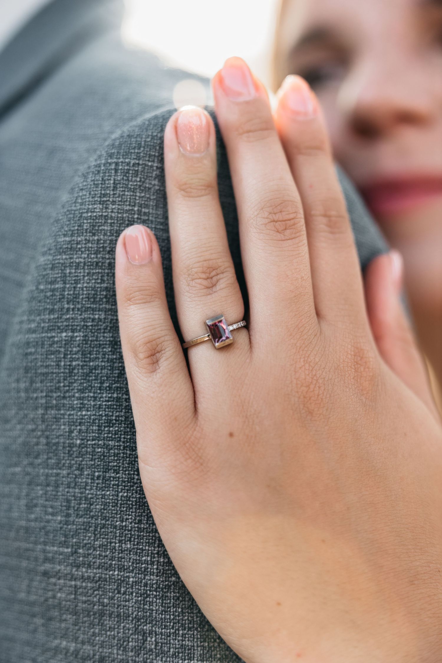Close-up of a bride's hand resting on groom's suit jacket, wearing an elegant purple gemstone ring.