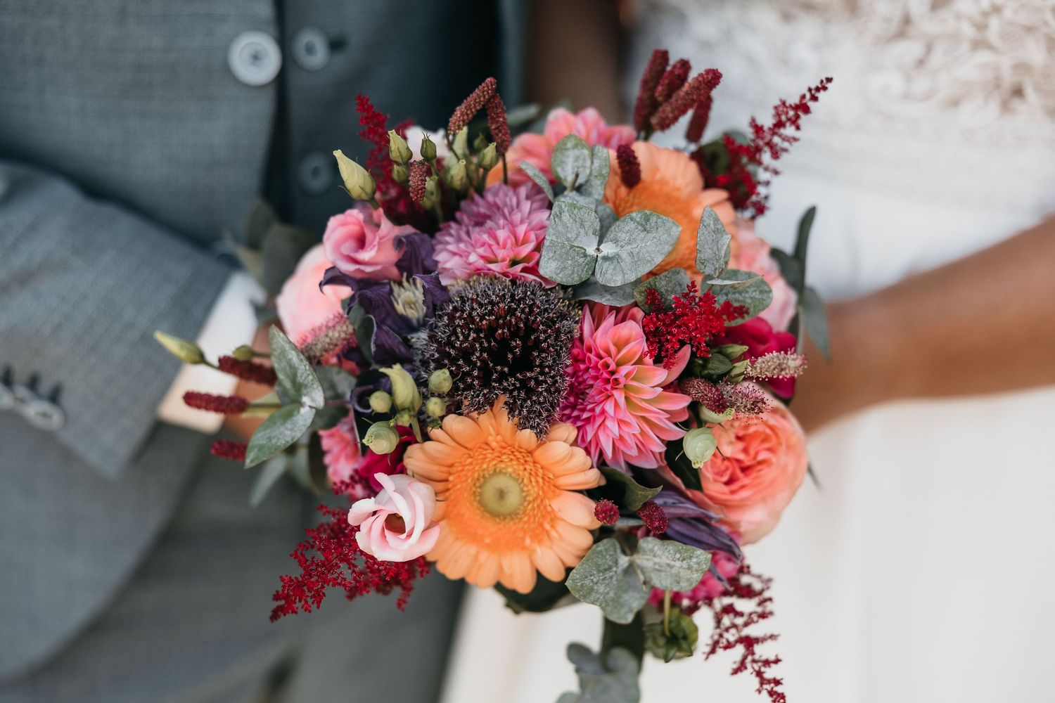 Close-up of a vibrant bridal bouquet with orange gerbera, pink roses, and deep red flowers.