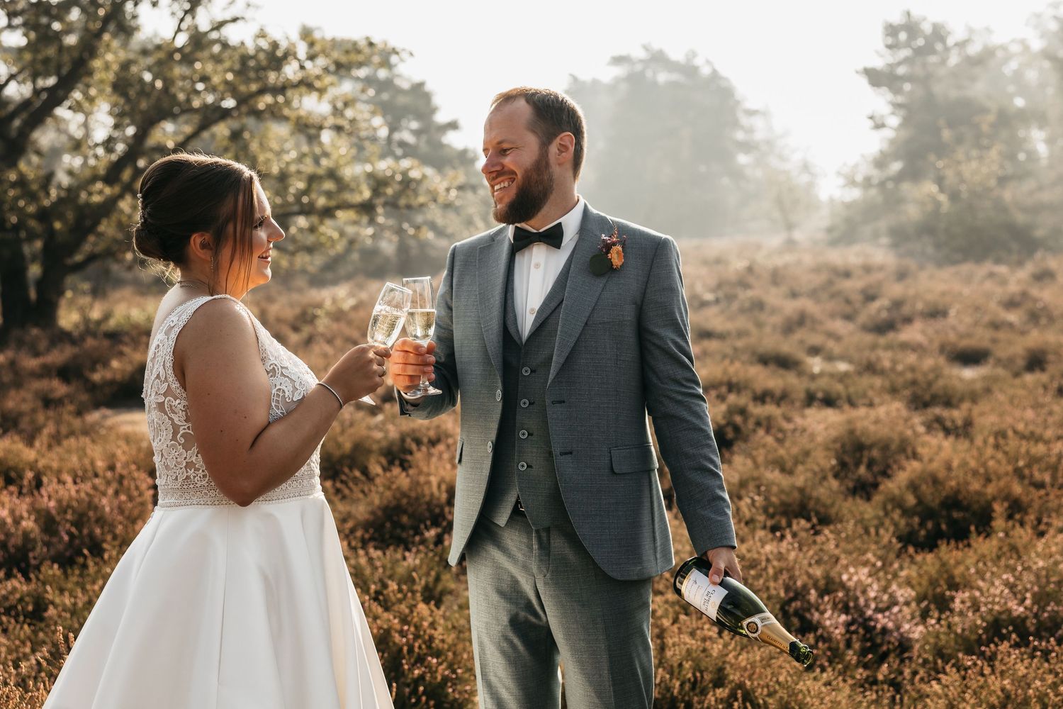 Bride and groom toasting with champagne glasses in a rustic autumn heather field at sunset.