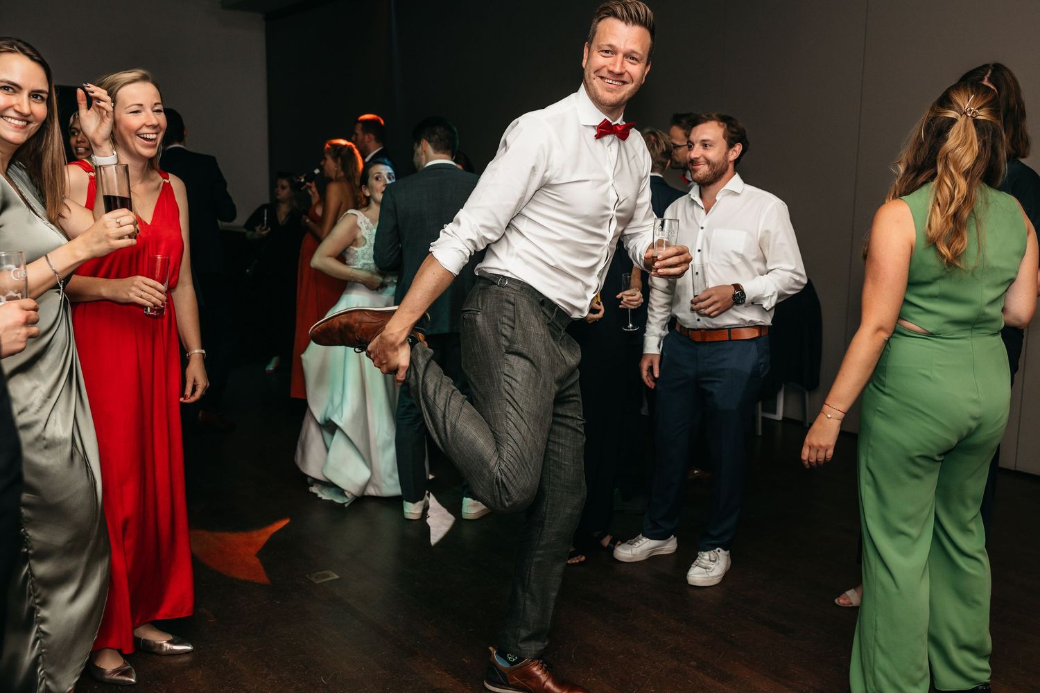 Man in white shirt and bow tie dancing energetically at wedding reception.